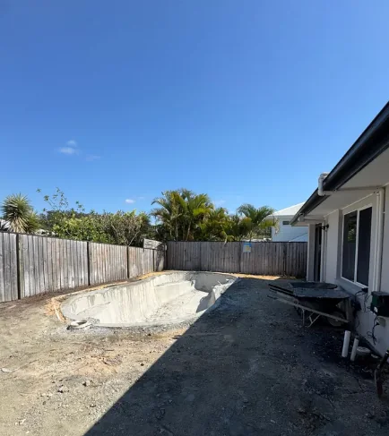 Partially demolished pool shell positioned beside a house with restricted access